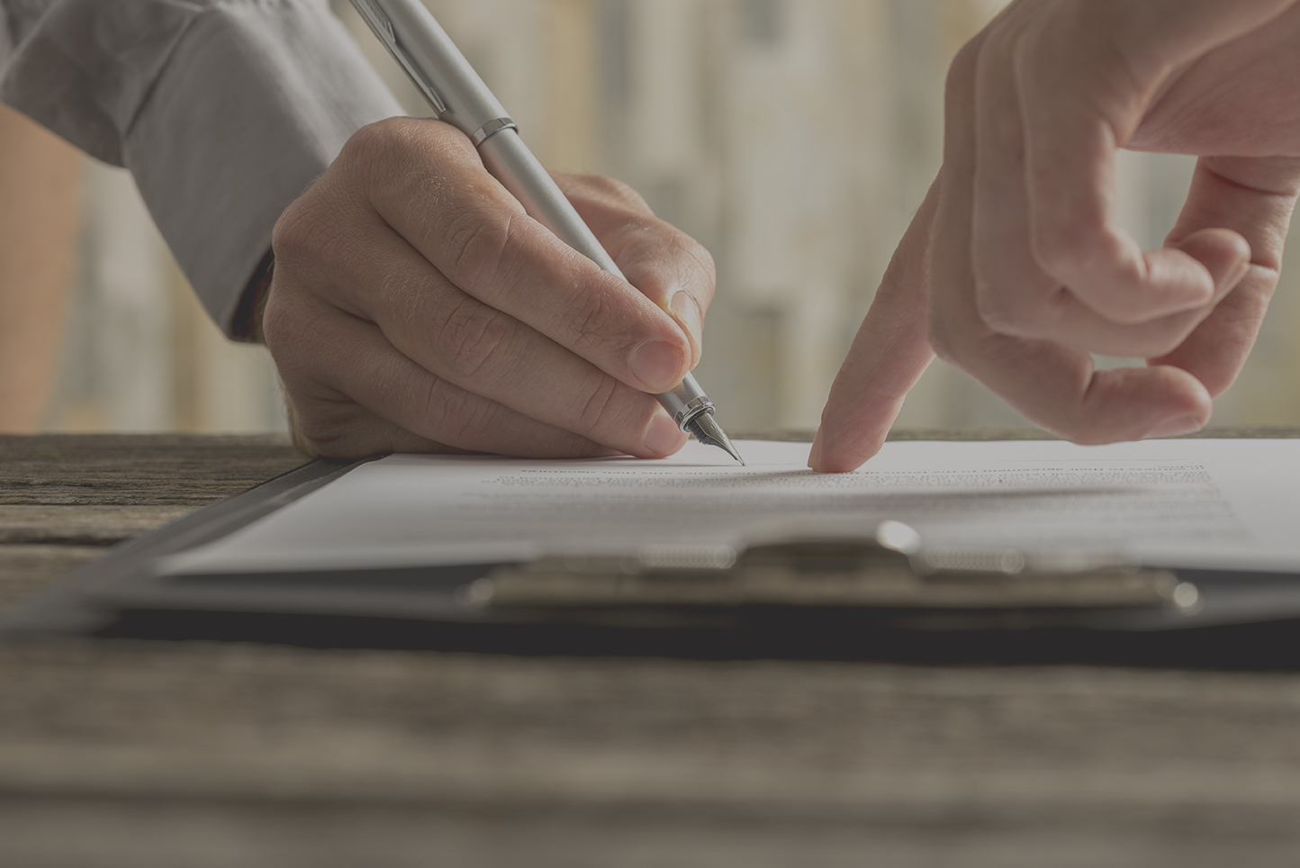 Closeup of businessman showing his new business partner where to sign an agreement or contract with fountain pen  on rustic wooden desk.